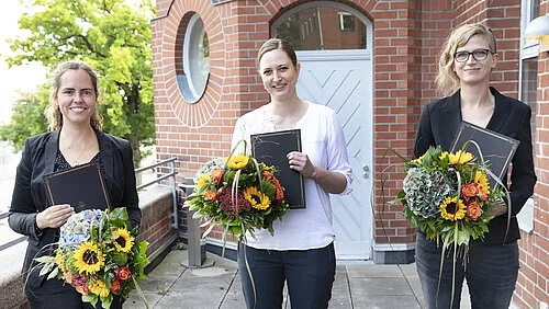 Drei junge Frauen mit Blumensträußen und Urkunden