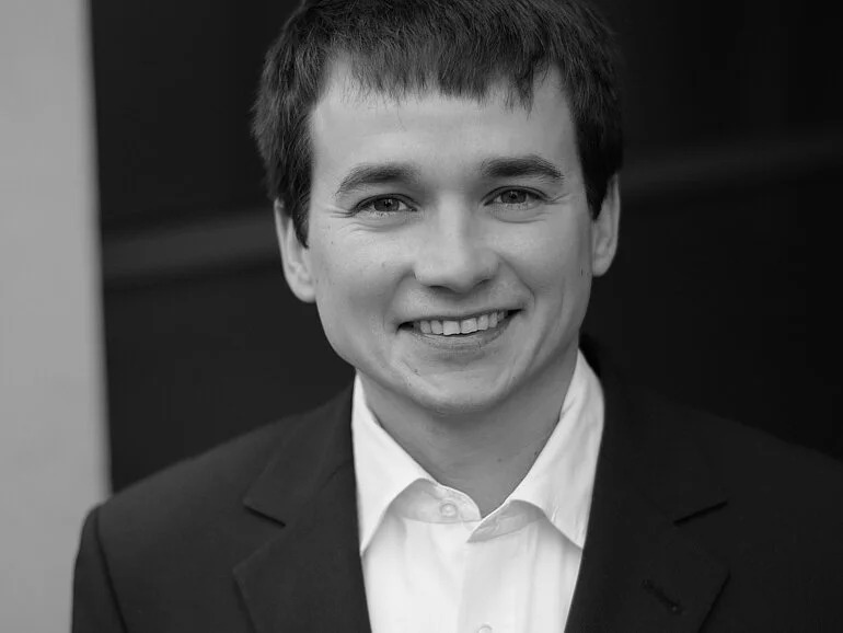Portrait: A young man with dark hair and a suit smiles at the camera.